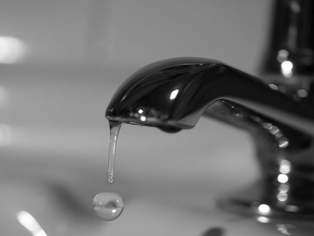 Foto em preto e branco de uma torneira com uma gota de água escapando.