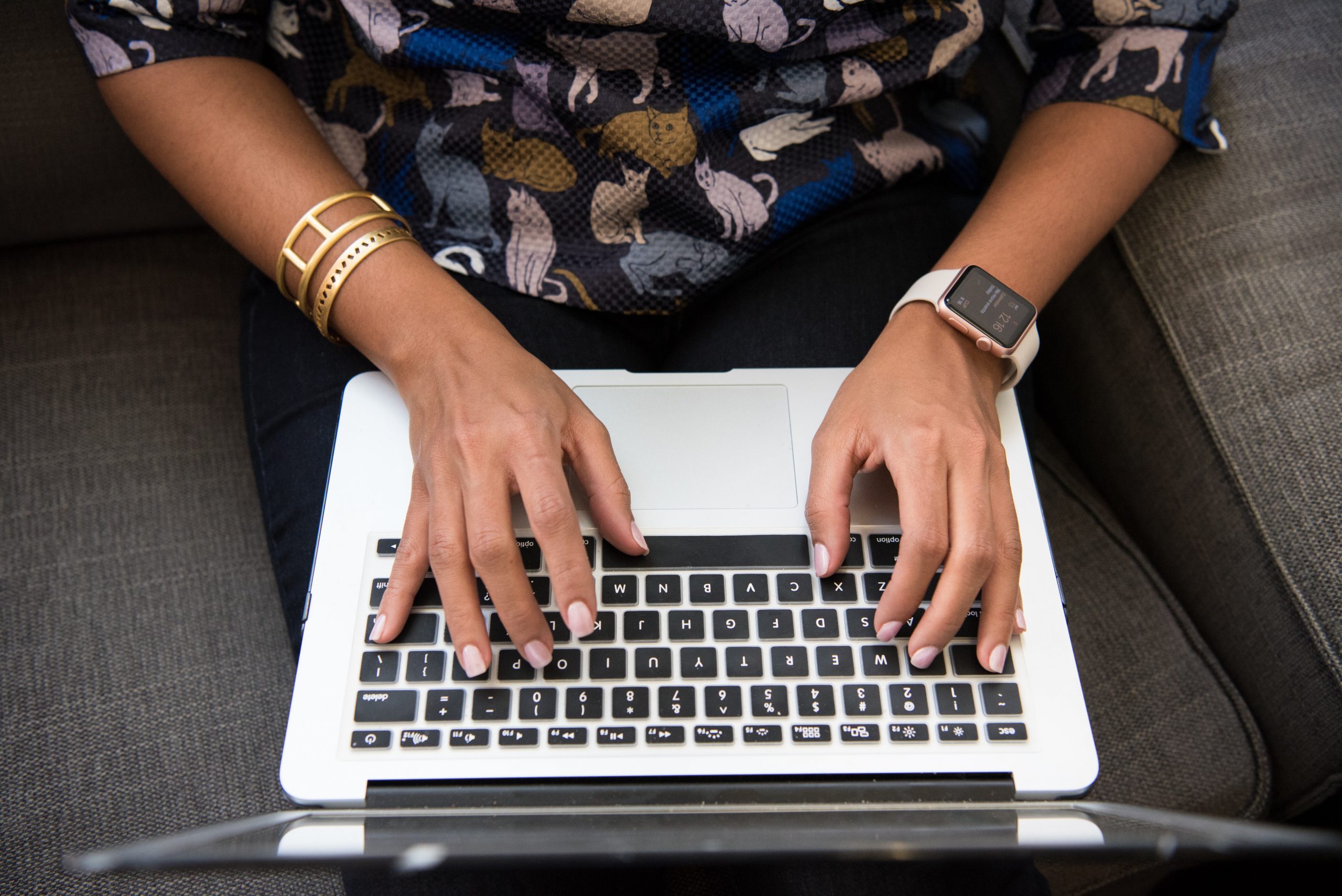 Imagem de uma mulher sentada no sofá com um laptop no colo, redigindo um texto.