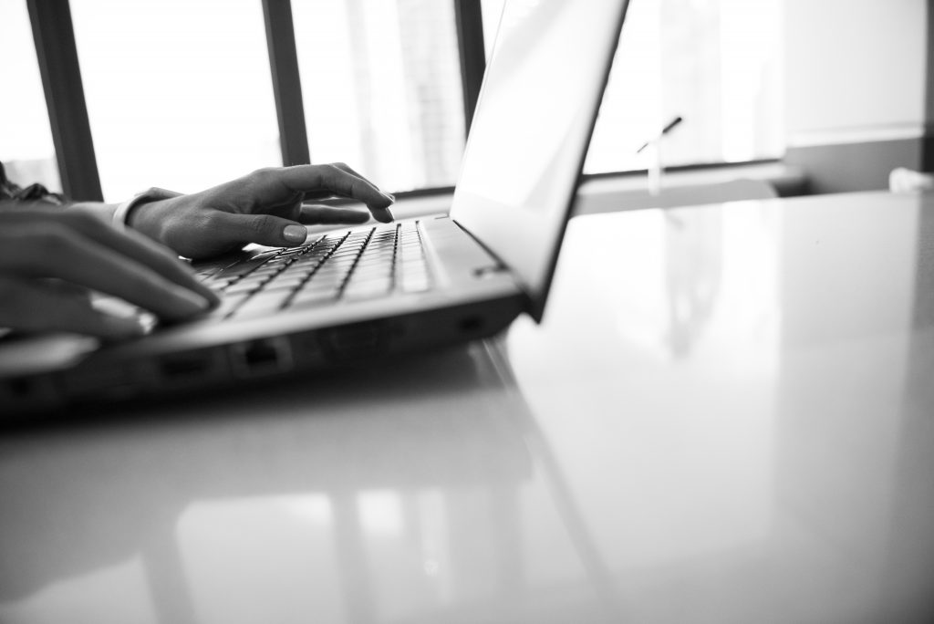 Imagem em preto e branco mostra duas mãos masculinas digitando num computador.